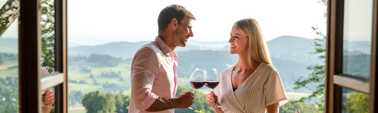 Pärchen genießt ein Glas Wein auf der Luxuschalet Bayern Terrasse mit Panoramablick über das Bergdorf Hüttenhof