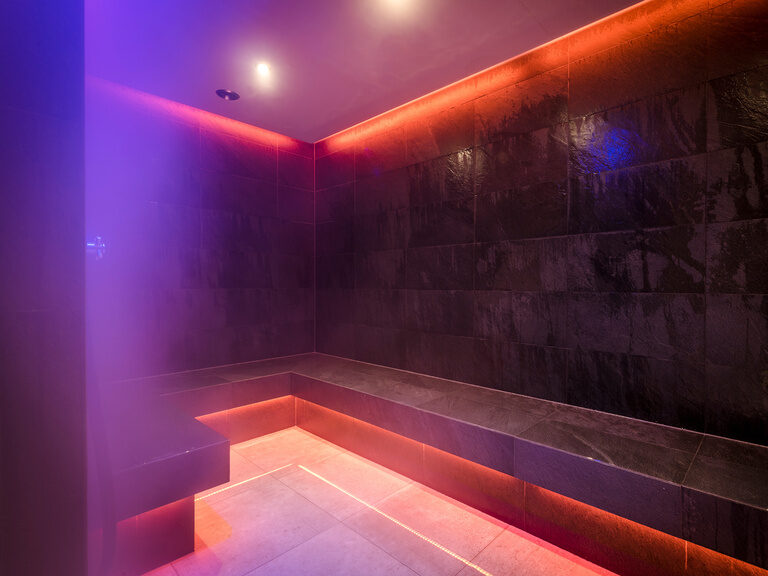 Modern gestalteter Raum mit Sitzbank für Aroma-Dampfbad, beleuchtet in warmen Rottönen