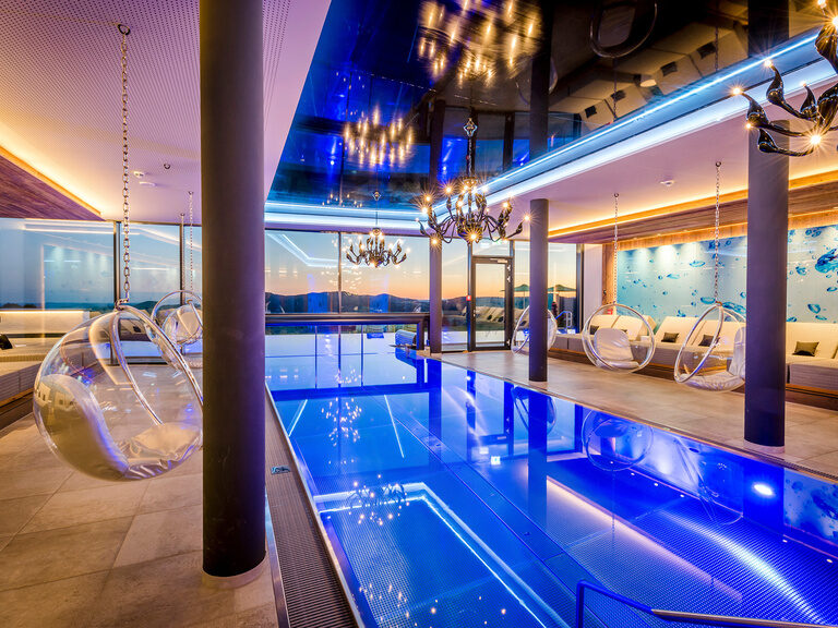 Außenansicht Hotel mit Außenpool, Liegen und Sonnenschirme auf Wiese mit Wald im Hintergrund