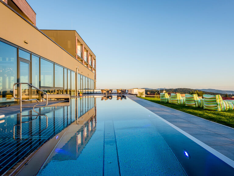 Außenpool bei Sonnenaufgang mit strahlend blauem Himmel und Blick auf den angrenzenden Garten mit Liegen