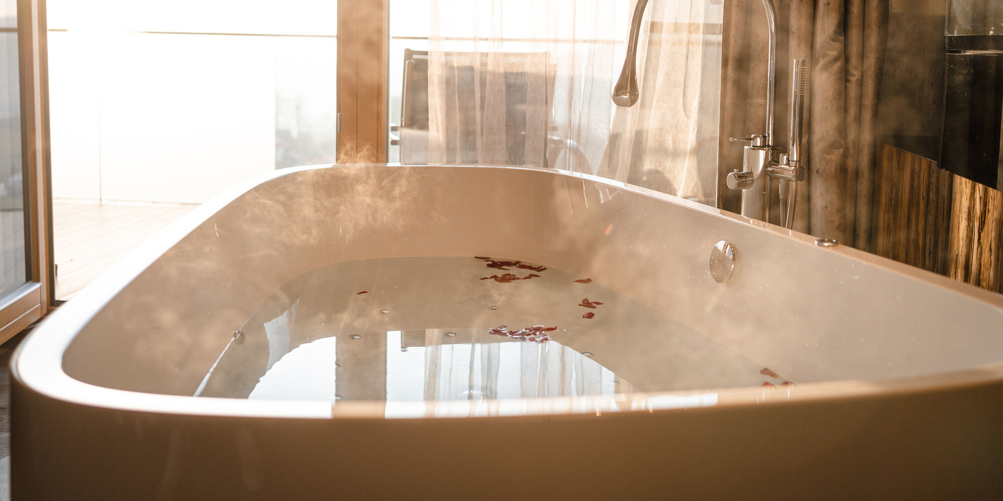 Freistehende Badewanne im Luxuschalet Bayern mit dampfendem Wasser und Rosenblüten