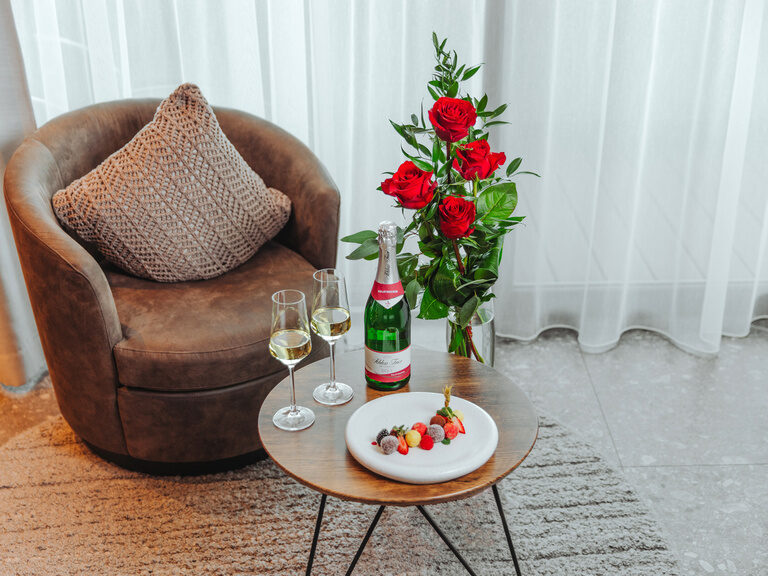 Befüllte Badewanne vor Kamin, mit Rosenblättern, darauf Holzbrett mit runden Badebomben