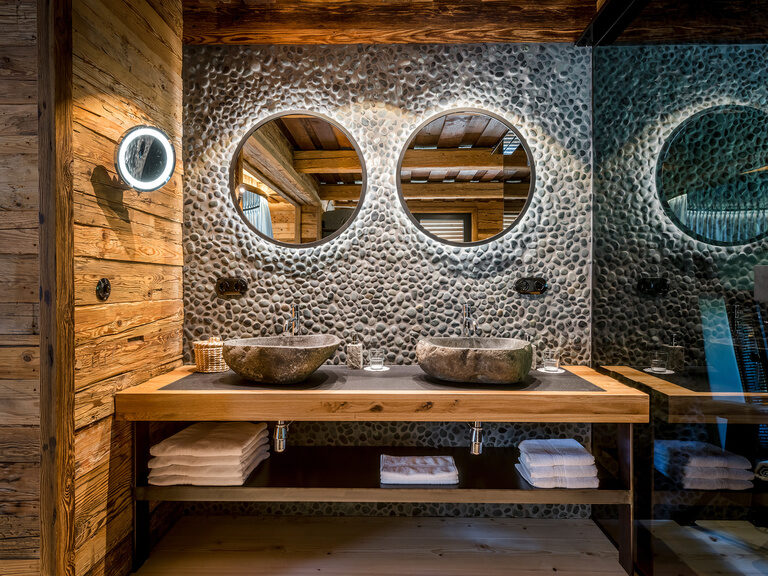 Badezimmer mit zwei Steinwaschbecken und runde Spiegel im Luxus Chalet Bayern