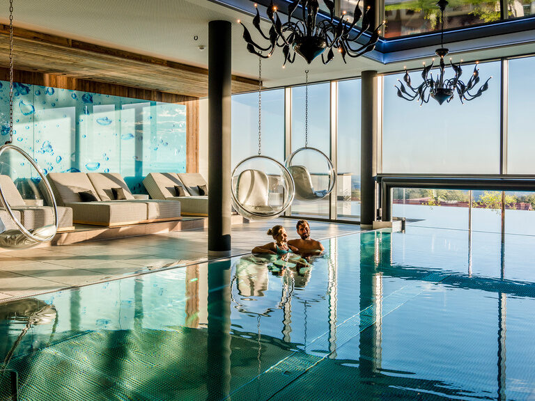 Beleuchteter, blauer Innenpool in der Dämmerung mit Panoramablick auf Bayerischen Wald