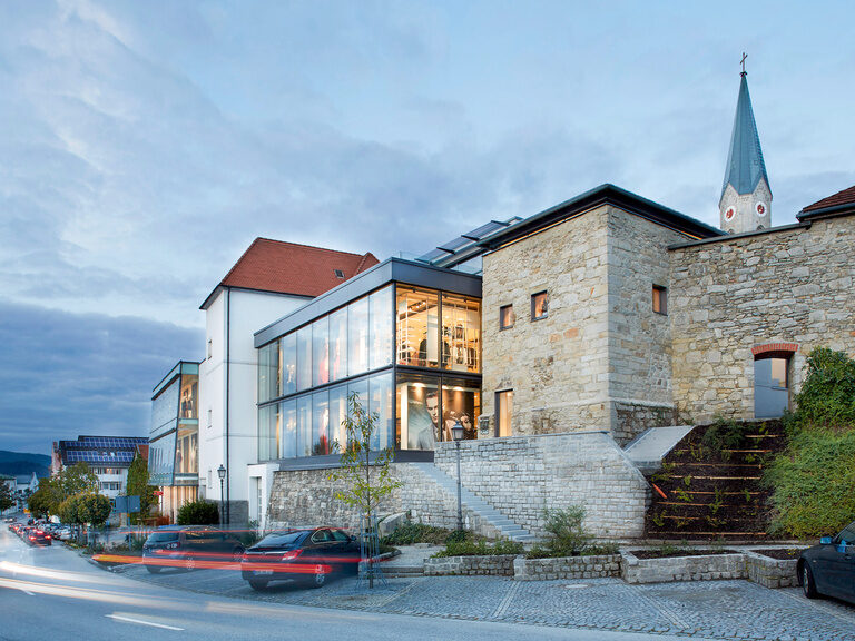 Blauer, beleuchteter Außenpool, umgeben von Liegen und Sonnenschirmen auf grüner Wiese