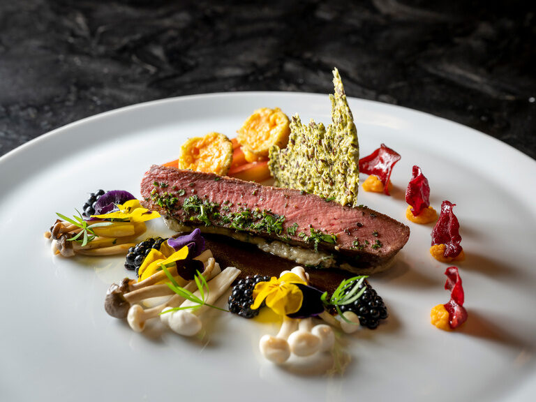 Blauer, beleuchteter Außenpool, umgeben von Liegen und Sonnenschirmen auf grüner Wiese