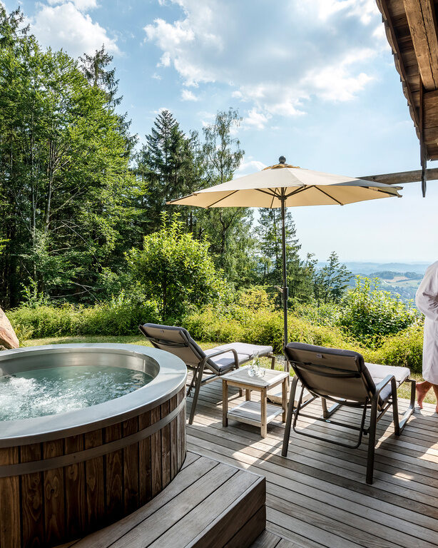 Pärchen im Bademantel steht auf Terrasse mit Whirlpool und Liegen des Luxus Chalets Bayerischer Wald