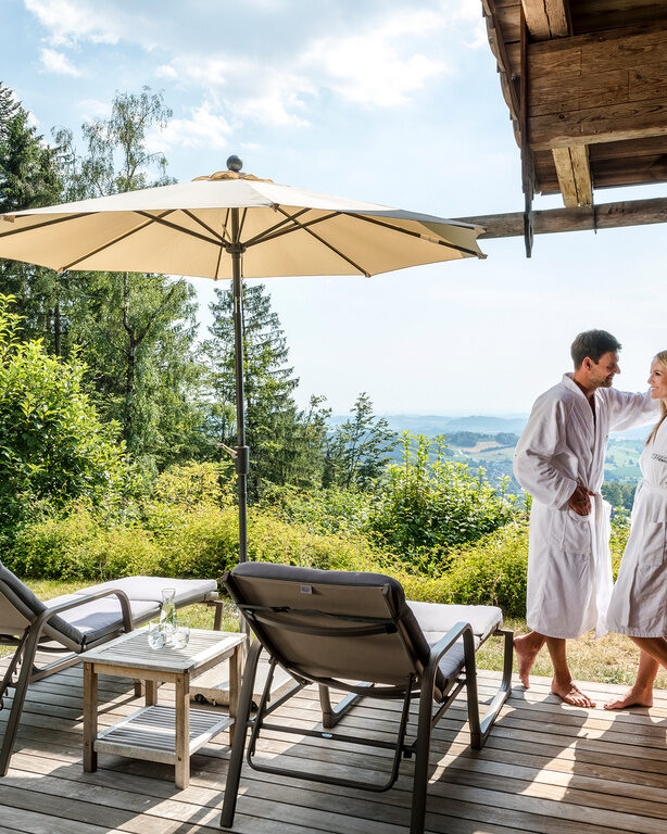 Pärchen im Bademantel steht auf Terrasse des Luxus Chalets Bayern mit Whirlpool und Liegen