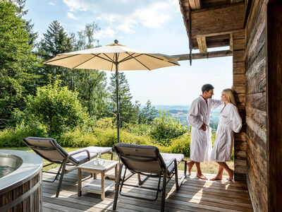 Pärchen im Bademantel steht auf Terrasse des Luxus Chalets Bayern mit Whirlpool und Liegen