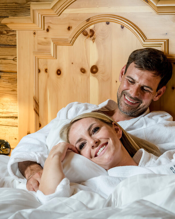 Pärchen kuschelt gemeinsam mit Bademantel im Bett des Luxus Chalets Bayerischer Wald