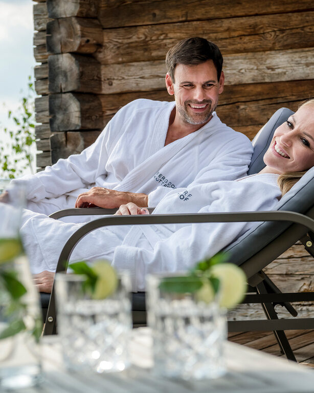 Pärchen genießt Wellnessurlaub Bayern auf den Liegen der Terrasse des Luxus Chalets Bayerischer Wald
