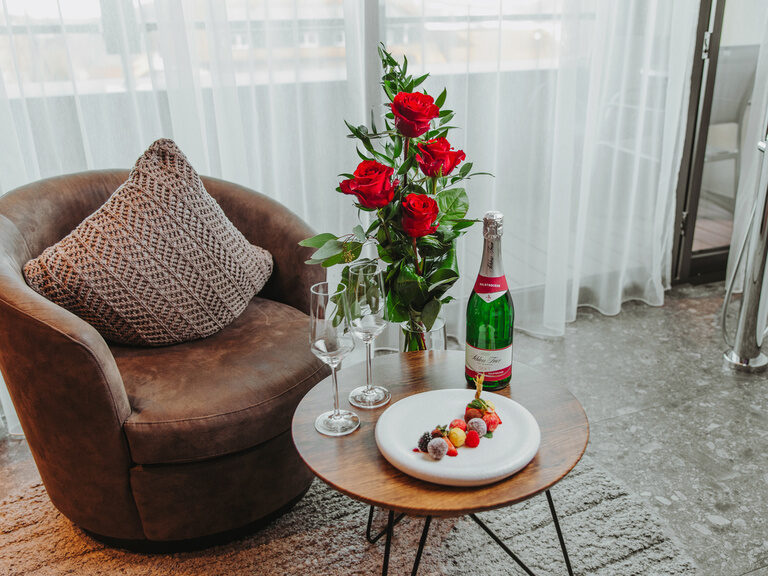 Rosenstrauß in Glasvase auf rundem Beistelltisch, Stoffsessel und rundes Bett im Hintergrund