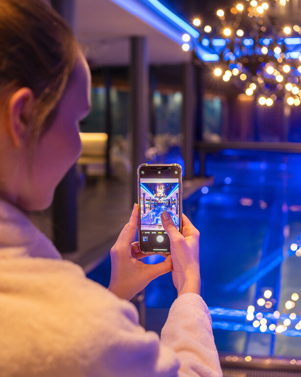 Frau macht Foto mit ihrem Smartphone vom Innenpool bei Nacht mit tollen Lichtern