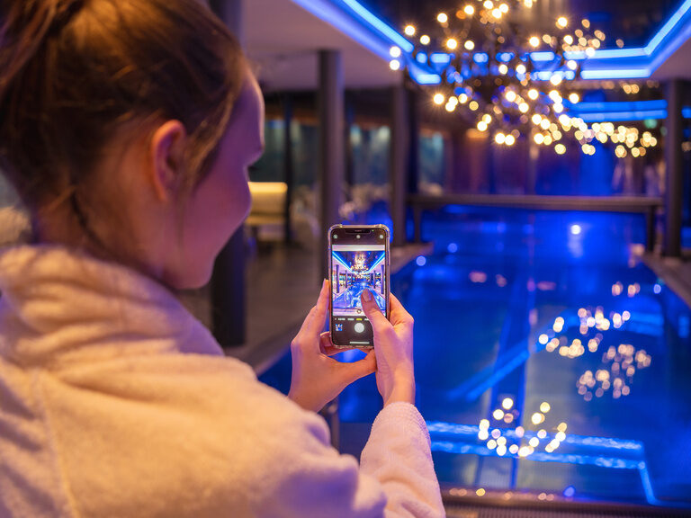 Frau macht Foto mit ihrem Smartphone vom Innenpool bei Nacht mit tollen Lichtern