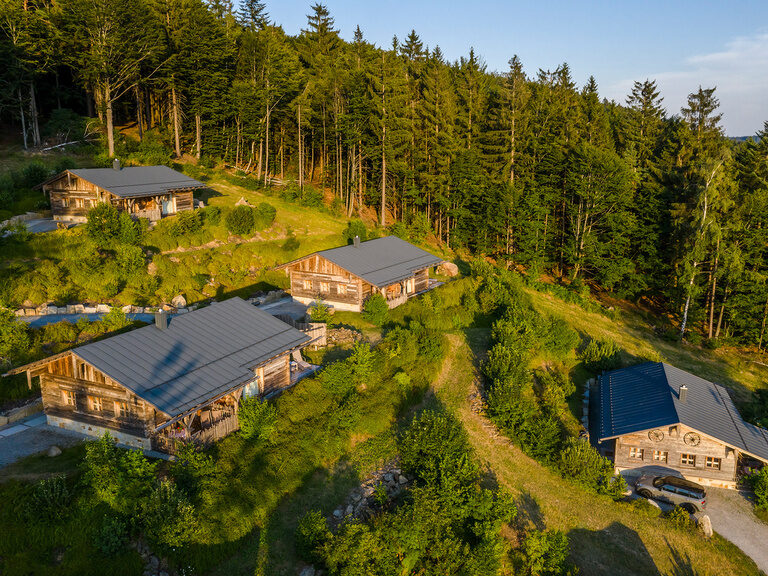 Luftaufnahme des Luxushotels Hüttenhof mit Dach- und Außenpool, umgeben von Wald