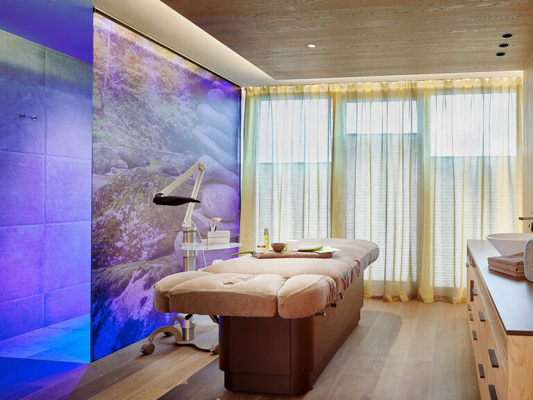 Moderner Spa-Behandlungsraum mit Beleuchtung an Wand, Liege und Waschbecken