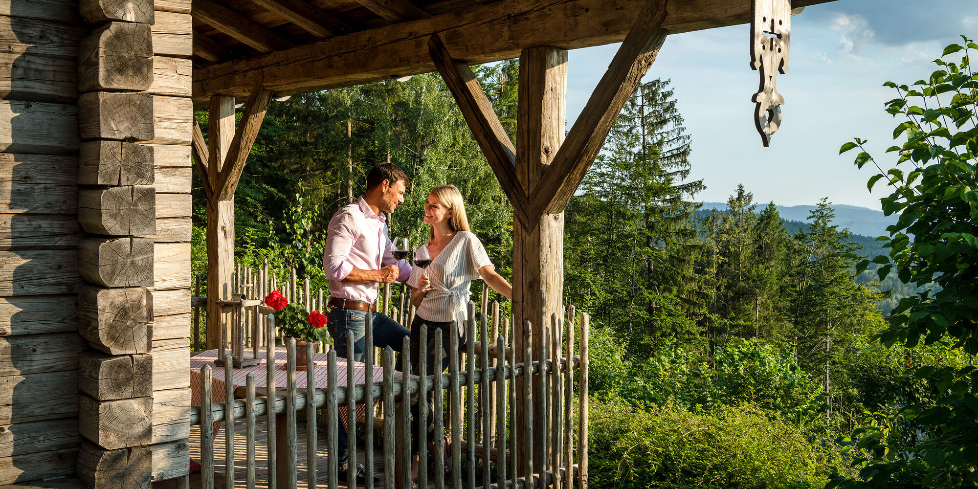 Pärchen genießt Wein auf Luxus Chalet Bayern Terrasse umgeben von Wald