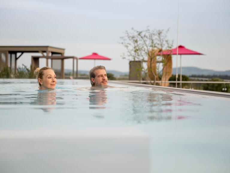 Pärchen schwimmt im Sky Pool im Hintergrund sind große Liegen zu sehen