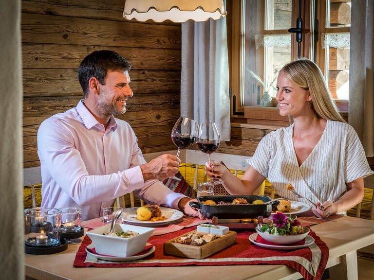 Pärchen sitzt am gedeckten Tisch mit einem köstlichen Bayerischen Gericht im Luxus Chalet Bayern