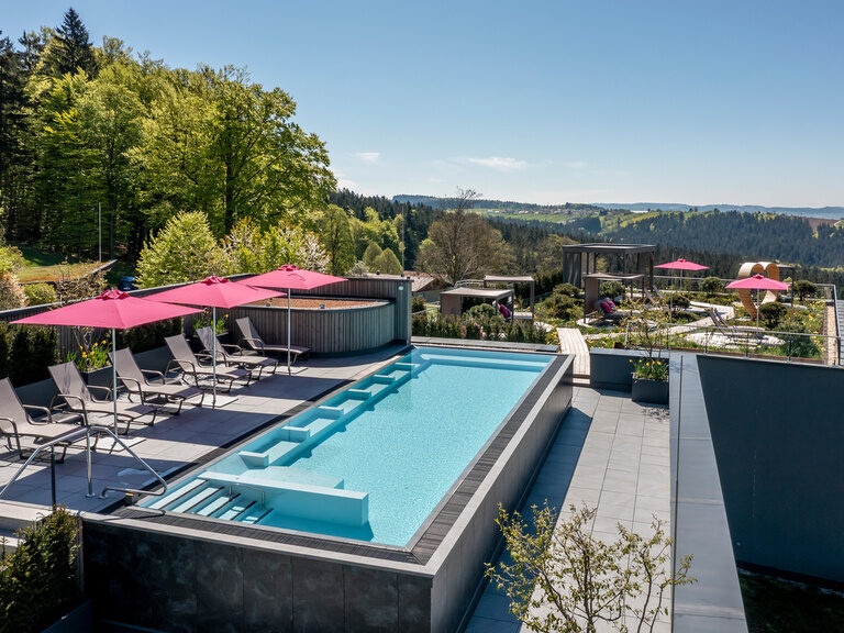 Pool auf sonniger Dachterrasse mit Sonnenschirmen und Waldpanorama vom Hotel Hüttenhof