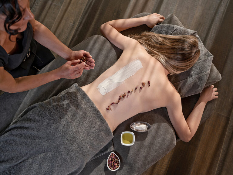 Obenansicht von Frau auf Behandlungsliege während Rücken-Spa-Behandlung, Kosmetikerin hält Zitrone in der Hand