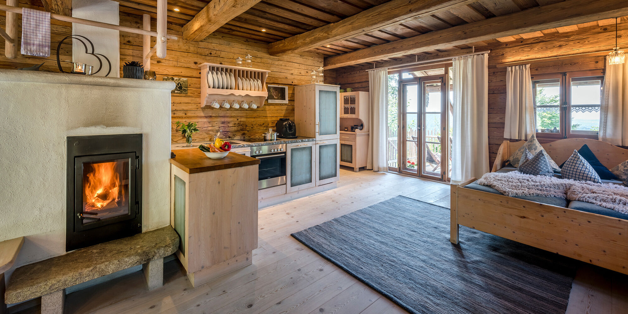 Wohnbereich mit Küche, Kachelofen und Bett im Luxus Chalet Bayern
